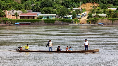 A boat with people passes by a tropical village surrounded by lush nature, people on boats near