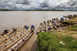 Wooden boats lie on the riverbank under a cloudy sky surrounded by lush greenery, longboat on a