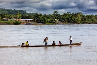 A long boat with people sails on a wide river with a green natural coastline, people on boats near