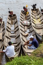 People sit in wooden barges with motors on the banks of a river, longboat on a river near