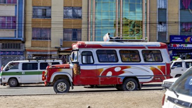 A red and white bus travels through a busy street surrounded by multi-colored buildings, traffic in