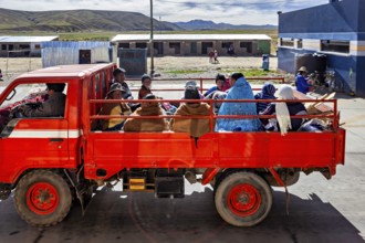 A red truck transports several people through a rural area in a quiet atmosphere, Road traffic in