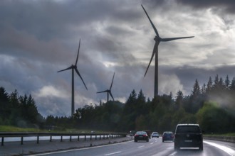Tourist traffic on the A9 motorway during thunderstorms, wind turbines in the pine forest in the