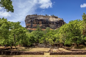 Historic ruins and lush greenery in front of an impressive rock under a blue sky, The Lion Rock