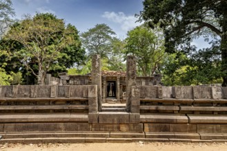 Stone gate marking the entrance to an ancient structure under a clear sky, surrounded by trees, The