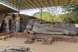 Panoramic view of a large reclining Buddha statue with a figure standing next to it under a