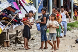 Group of people, including woman and children, stand at a market with colorful stalls, poverty in