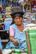 A thoughtful woman in traditional traditional costume sits in front of a colorful market stall, The