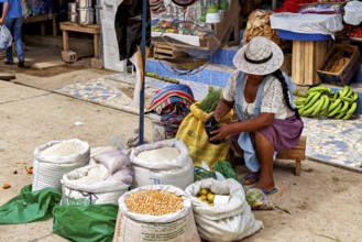 Woman wearing a hat sitting at the market and opening a bag of grain, The Rurrenabaque market in