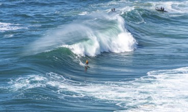 Surfers with their jet ski pilots in the Atlantic waves below Farol de Nazaré, Forte São Miguel,