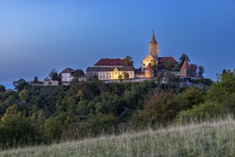 An illuminated castle on a hill at dusk, surrounded by shady trees, The Leuchtenburg near Kahla im