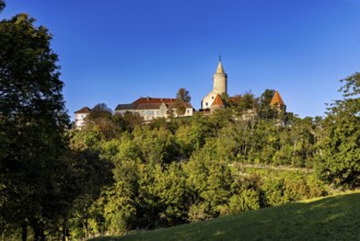A castle on a wooded hill with clear blue sky in the background, The Leuchtenburg near Kahla im