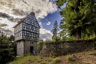Half-timbered house on a stone base next to a stone wall in the forest, picturesquely illuminated