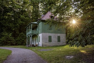 Green house in the forest with evening sun, quiet path and wooden veranda in peaceful surroundings,