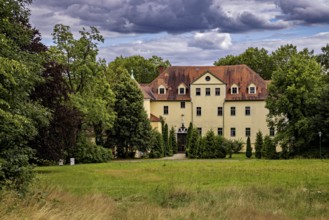 Manor house surrounded by green trees and meadows, under a cloudy sky, The Hummelshain hunting