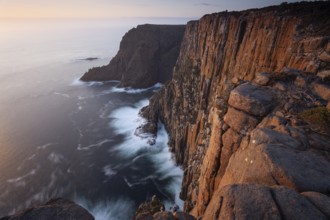Long exposure shows sunset over the cliffs of Cape Raoul. Golden light hits the sea and colors the