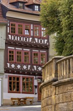 A half-timbered house with red window frames next to a stone wall in a historic town, The old town