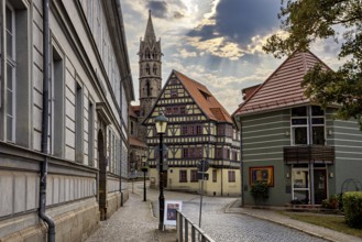 Paved street with half-timbered houses and church tower under a cloudy sky, the old town of
