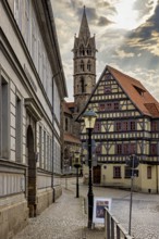 Alley with a view of a half-timbered house and a church tower, under a cloudy sky, the old town of