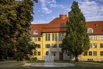 Large yellow building with surrounding garden, fountain and summer backdrop, the old town of