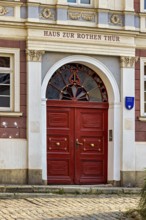 Red door in a historic building with decorative stone elements and symmetrical decorations, door to