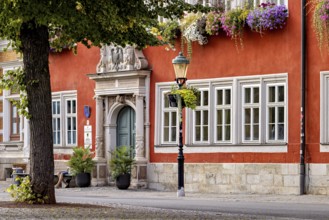 Red façade with blooming flowers and lantern next to an ornate entrance in the old town, The old