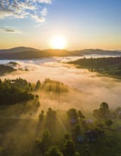 Sunrise over a fog covered village in a rural landscape, golden morning light, serene autumn