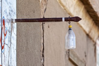 A plastic bottle with a light bulb hangs from an old metal rod on a wall, street lamp in the town