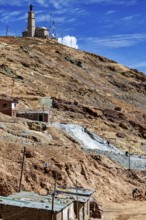 Church on a mountain in a barren, dry landscape with antennas and stone houses under a blue sky,