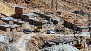 Several clay-coloured houses in a mountainous landscape with parked cars and rubble, The silver
