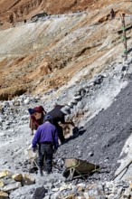 Workers bend on a rocky slope while loading gravel into wheelbarrows, The silver mines of Potosi