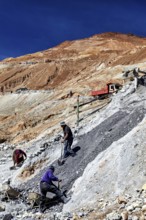 A worker shovels stones down a hill, accompanied by an arid landscape, The silver mines of Potosi
