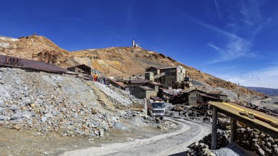 Old industrial complex in a mountainous environment under a clear blue sky with a visible path, The