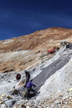 Workers shovelling on a stony slope under a clear blue sky, The silver mines of Potosi Bolivia