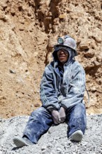 A miner in dusty clothing sits in front of a rock face near a mine, The miners of the Cerro Rico