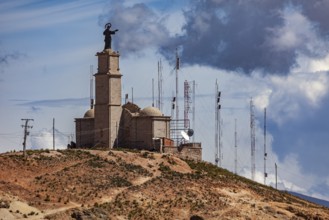 A hill with a large statue and several radio towers against a cloudy sky, The church on the Cerro