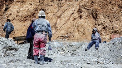 Miners in different clothes stand or sit in a barren, dusty environment, The miners of the Cerro