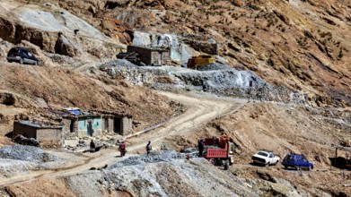 Stone houses on a dirt road with passing cars and mining scenes, The silver mines of Potosi Bolivia