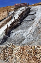 A lonely mine car stands on a rocky slope, surrounded by staggered layers of rock and wooden beams,