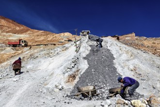 Workers with wheelbarrows on a stony slope under a bright blue sky, The silver mines of Potosi