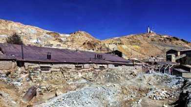 Old, dilapidated mining structures in front of a dry hill under a clear sky, The silver mines of
