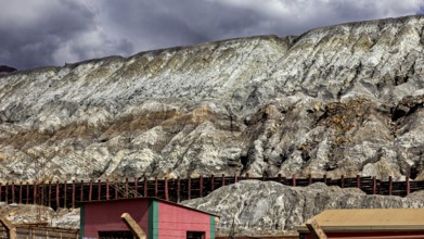 Industrial landscape with buildings at the foot of steep rock faces under a cloudy sky, slag heap