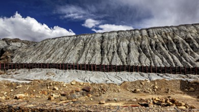 Steep rock faces in a barren desert landscape with clouds in the sky, spoil heap of the silver