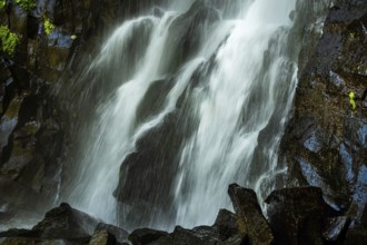 Vaucoux waterfall cascades gracefully over dark rocks, surrounded by lush greenery, Auvergne