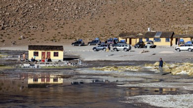 Huts and vehicles in a mountainous landscape with people, The thermal springs of Polques in Bolivia