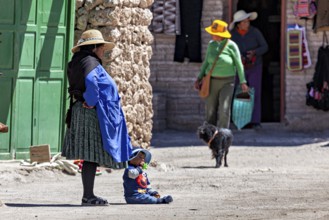 Woman and child in traditional dress stand with a dog in front of a green door in the village,