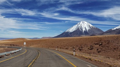 Deserted road leads to a snow-covered mountain under a clear sky, The landscape with the volcanoes