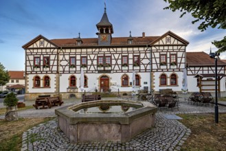 Half-timbered building with fountain and seating on cobblestone square at dusk, Historic