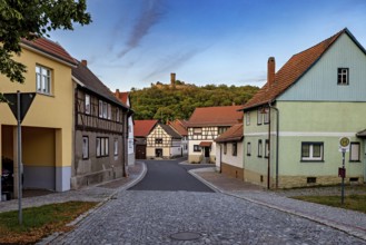Historic village with half-timbered houses, castle ruins on a green hill and cobbled street, the
