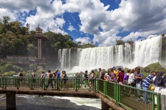 Tourists on a bridge watch the impressive waterfalls in the background, The Iguazu Falls between
